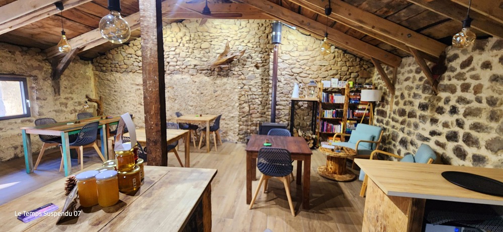 Intérieur du restaurant avec des tables en bois, un mur en pierres, des chaises confortables et une bibliothèque remplie de livres ainsi que des jeux à dispositions 